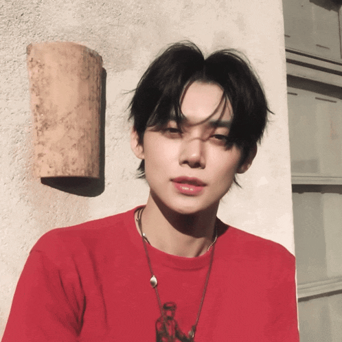 a young man wearing a red t-shirt is standing in front of a wall