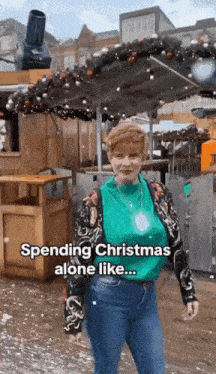 a woman in a green sweater and jeans is standing in front of a christmas decoration .