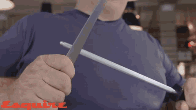 a man in a blue shirt is holding a knife in front of a sign that says esquire on it