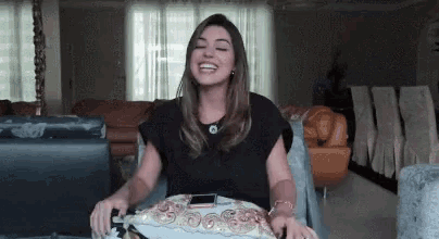 a woman is sitting on a couch in a living room laughing while holding a plate .