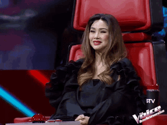 a woman in a black dress is sitting in a red chair on the voice indonesia show .