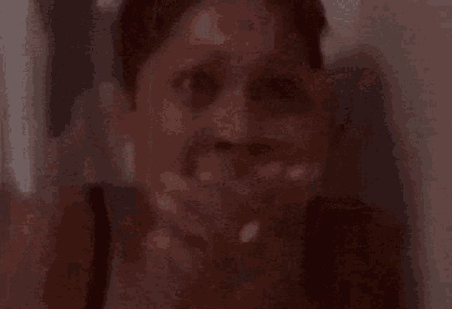 a woman is covering her mouth with her hands in a dark room