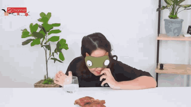 a woman wearing a blindfold sits at a table holding a glass