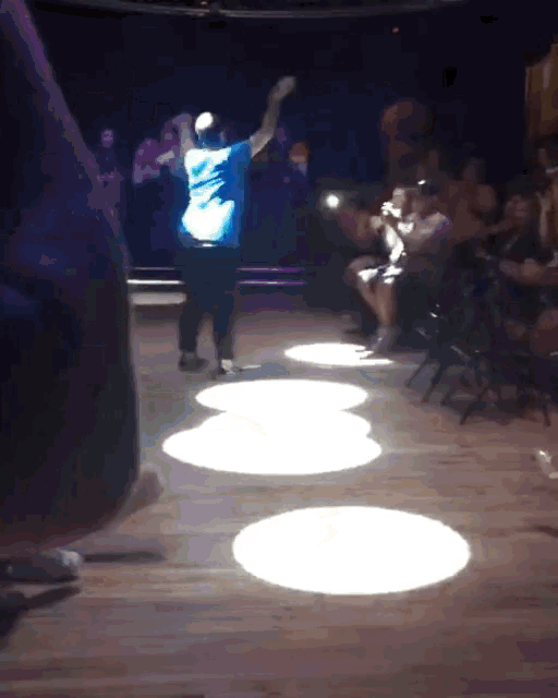 a man in a blue shirt is dancing in front of a crowd of people
