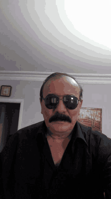 a man wearing sunglasses and a mustache is standing in front of a clock