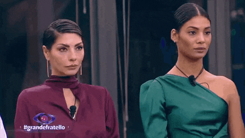 two women are standing next to each other in front of a sign that says grandefratello on it