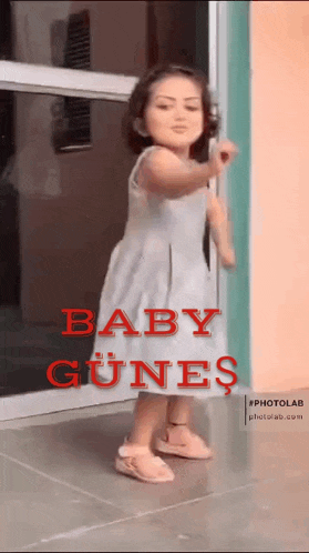a little girl in a white dress is standing in front of a door with the words baby gunes on it