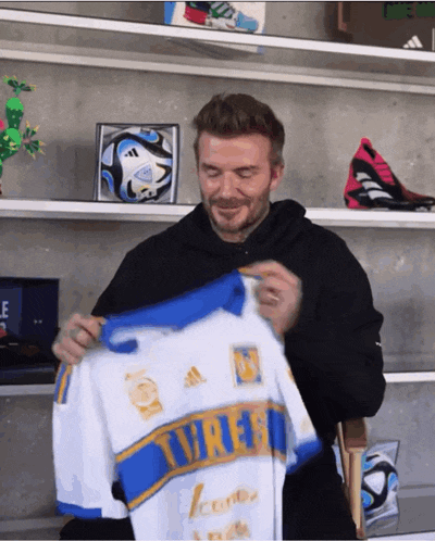 a man in a black hoodie is holding a white and blue jersey that says tigres