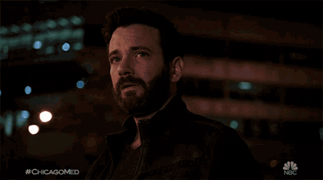 a man with a beard is standing in front of a nbc sign