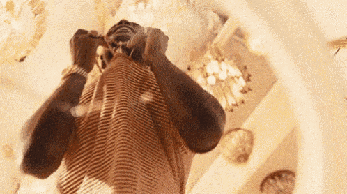 a man is covering his face with his hands in a room with a chandelier .