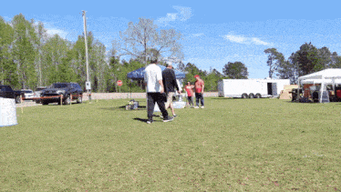 a group of people standing in a grassy field with a white trailer in the background