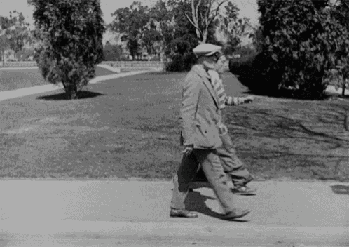 a black and white photo of two men walking down a sidewalk in a park