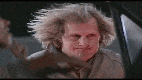 a man with very long blonde hair is sitting in a car with his hair blowing in the wind .