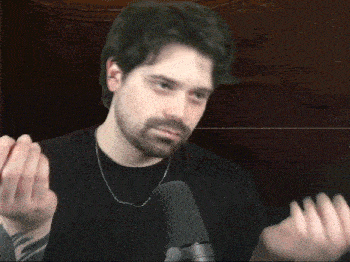 a man with a beard stands in front of a microphone with his hands up