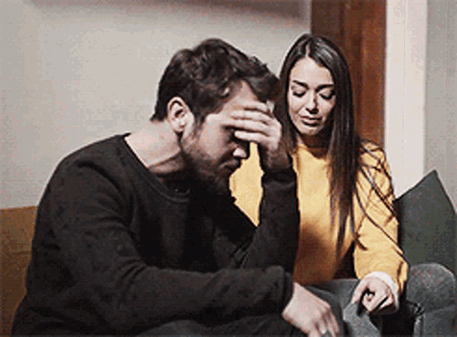 a man and a woman are sitting on a couch . the man is covering his face while the woman looks on .