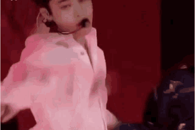 a man in a pink shirt is dancing on a stage with a microphone in his mouth .