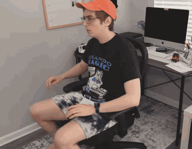 a man wearing an orlando magic t-shirt sits in a chair