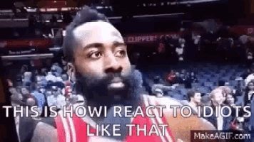 a basketball player with a beard is sitting in the stands at a basketball game and making a funny face .