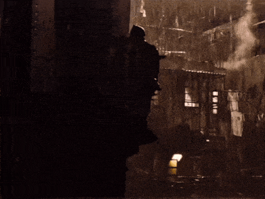a silhouette of a person standing in the rain with smoke coming out of a building