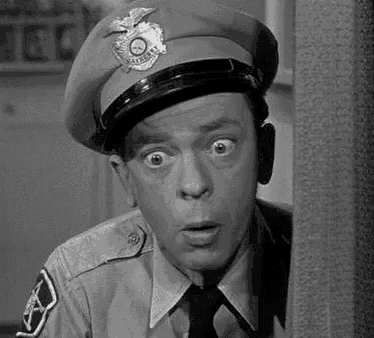a black and white photo of a man in a police uniform and tie making a funny face .