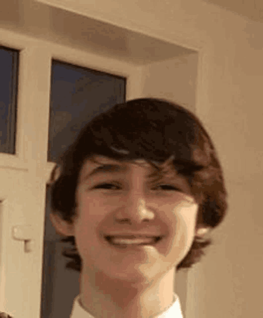 a young boy is smiling for the camera while wearing a white shirt and tie .