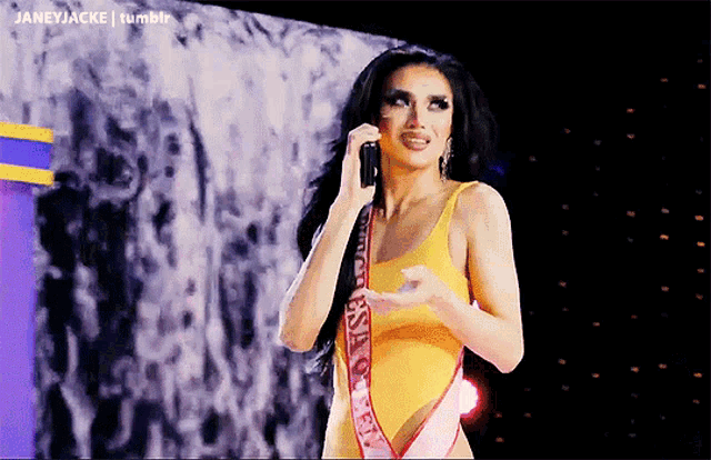 a woman in a yellow swimsuit with a sash that says usa on it is talking on a cell phone