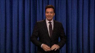 a man in a suit and tie stands in front of a blue curtain with his arms outstretched