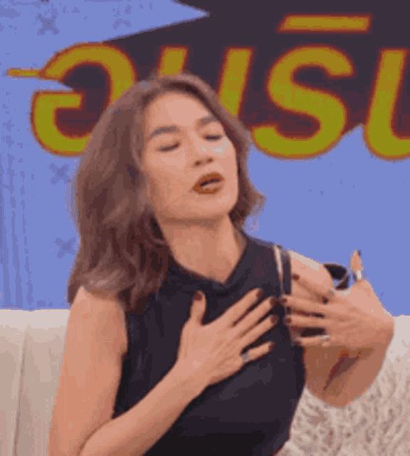 a woman in a black top is sitting on a couch with her hands on her chest ..