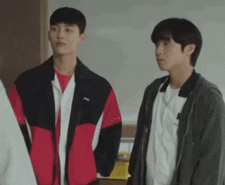 two young men are standing next to each other in a room and talking to each other .
