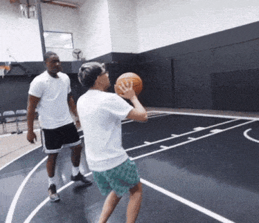 two men are playing basketball on a court and one is holding a basketball in his hand