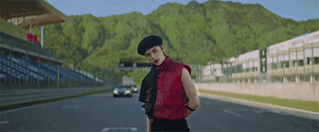 a man in a red vest and black beret is standing on a road .