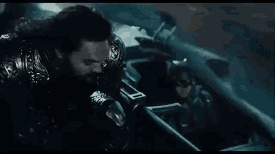 a man with a beard is sitting in a car with the words `` gue nebeng ya '' written on the screen .