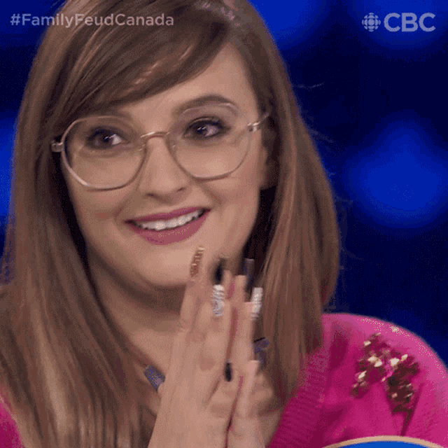 a woman wearing glasses and a pink sweater is smiling and clapping her hands in front of a blue background that says cbc