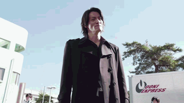 a man in a trench coat stands in front of an odori express truck
