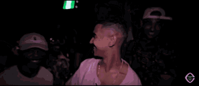 a man in a pink shirt is dancing in a dark room while another man looks on .