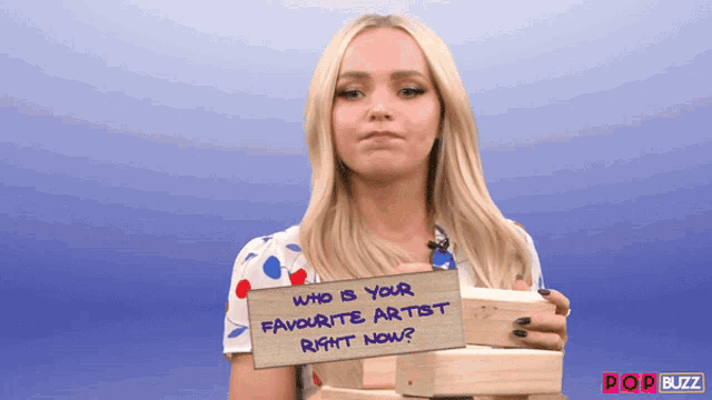 a blonde woman holding a sign that says who is your favorite artist right now