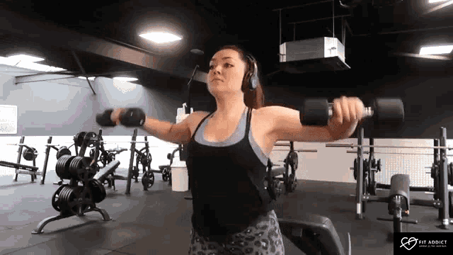 a woman in headphones is lifting dumbbells in a gym .