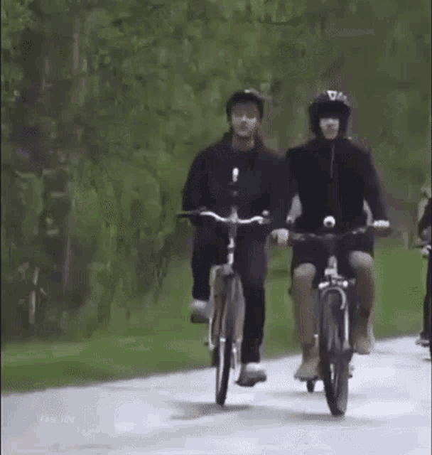 two people are riding bicycles down a road in the park .