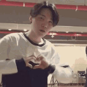 a young man is making a heart with his hands in a room .