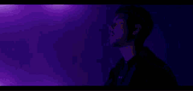 a man in a black jacket is standing in front of a purple background .