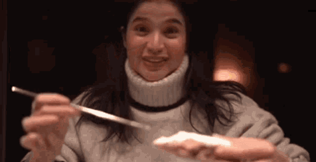 a woman wearing a turtleneck sweater is holding a fork in her hand