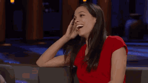 a woman in a red shirt is sitting on a couch and smiling .