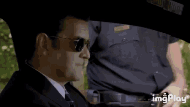 a man wearing sunglasses is sitting in a car with a police officer .