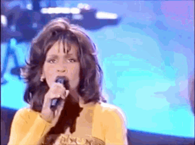 a woman singing into a microphone while wearing a yellow top
