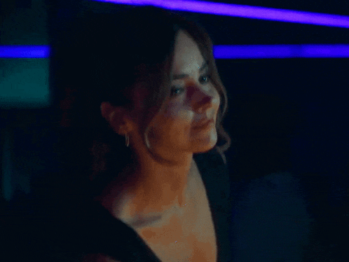 a woman in a black dress is standing in a dark room with purple lights .