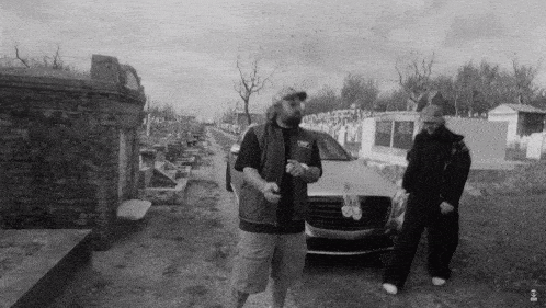 a black and white photo of two men standing next to a silver car