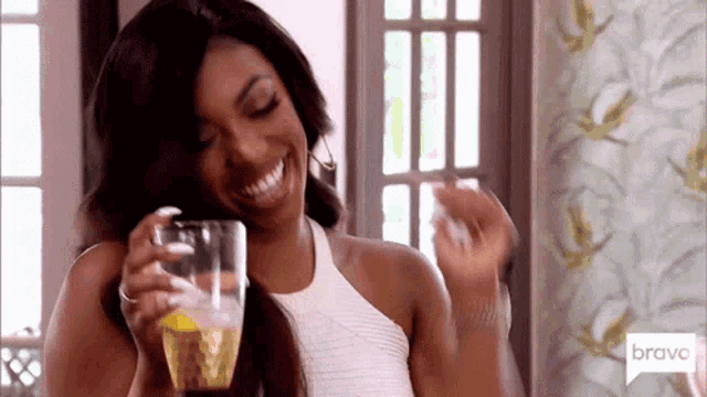 a woman in a white tank top is holding a glass of wine and smiling .
