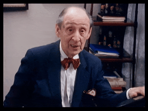 a man in a suit and bow tie is sitting in front of a book shelf