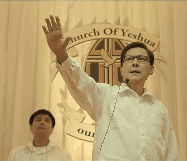 a man is giving a speech in front of a microphone in a church while another man watches .