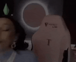 a close up of a woman 's face with a green object on her head and a pink chair in the background .